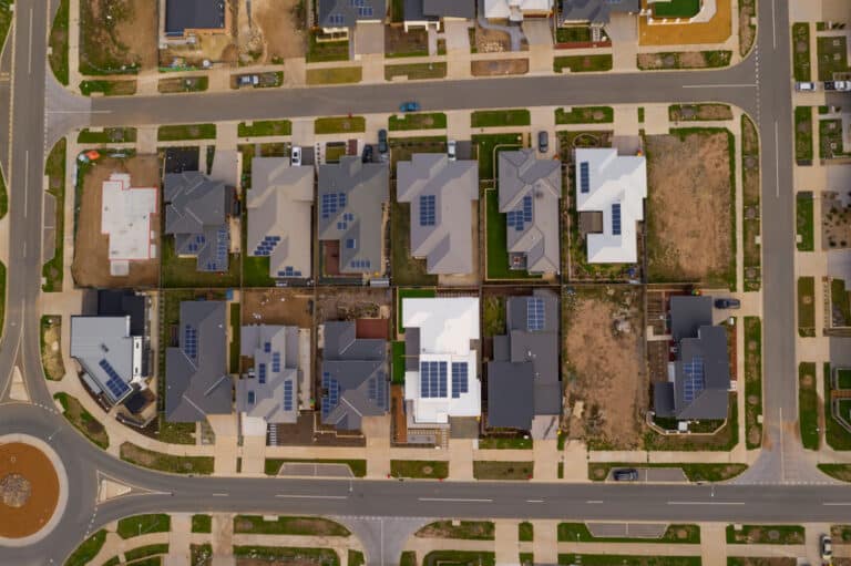 The image shows an aerial view of a suburban neighborhood with multiple houses featuring solar panels on their roofs.