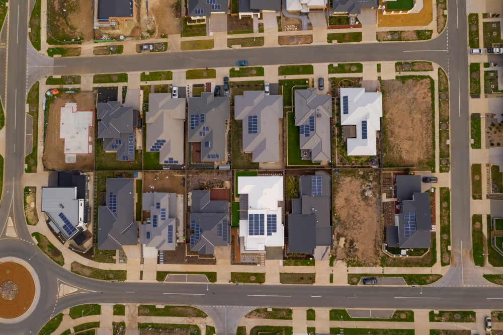 The image shows an aerial view of a suburban neighborhood with multiple houses featuring solar panels on their roofs.