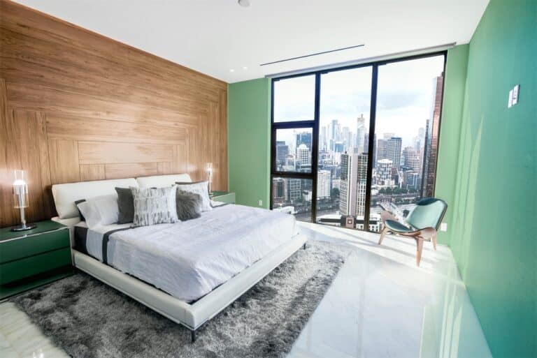 A bedroom with green walls featuring a large window that offers a view of the city skyline.
