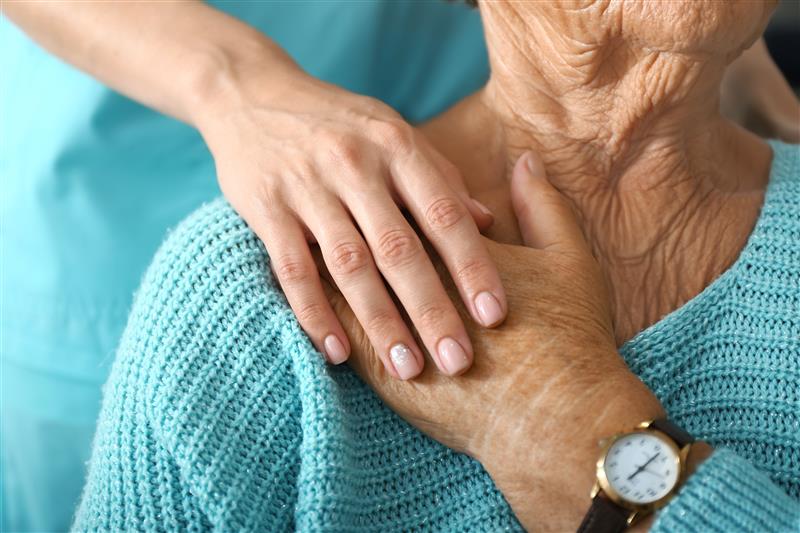 A nurse gently holds the hand of an elderly woman, providing comfort and support in a caring environment.
