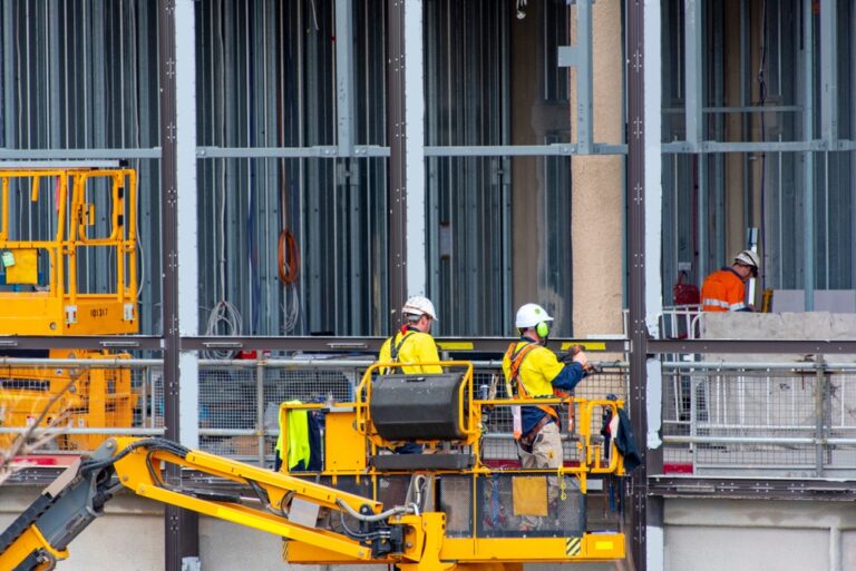 Construction workers wearing hard hats and safety vests collaborate on a busy construction site with machinery in the background.
