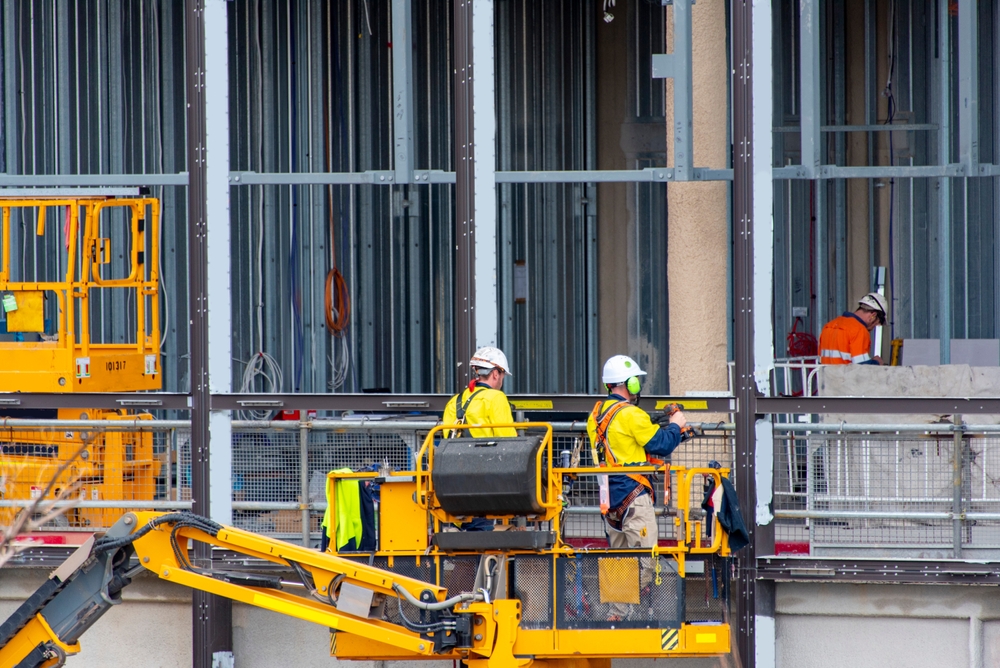Construction workers wearing hard hats and safety vests collaborate on a busy construction site with machinery in the background.