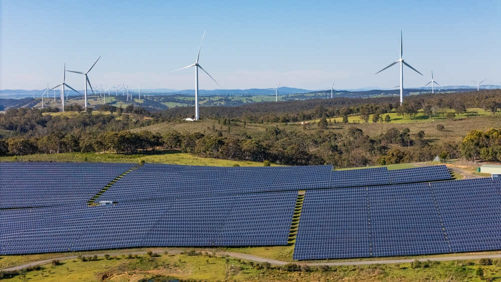 Aerial drone view of a hybrid solar and wind farm showing the large wind turbines in the background for renewable clean energy supply located at Bannister, NSW, Australia on a sunny day